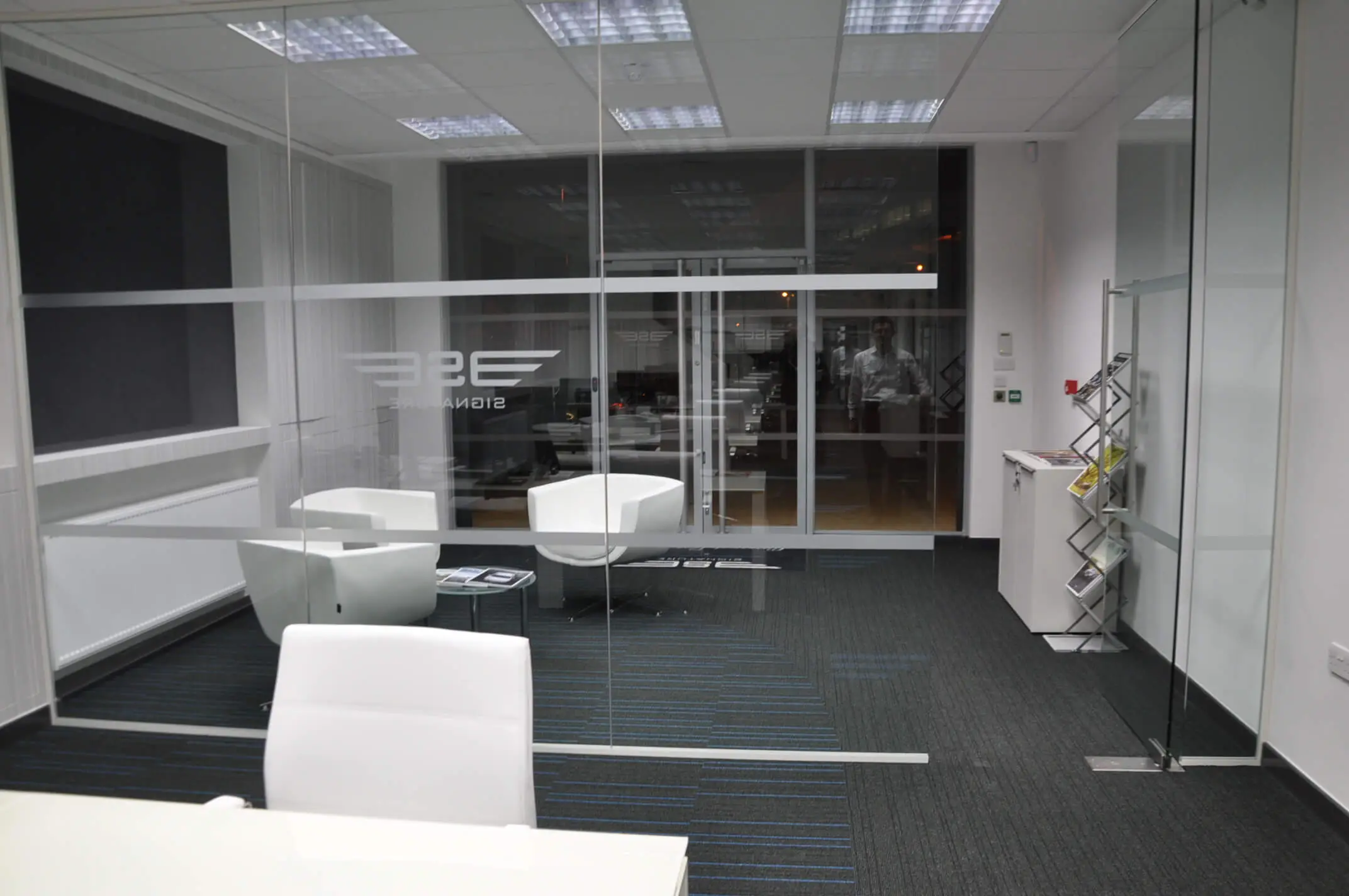 Breakout space in office with armchairs coffee table and frameless glass partitions