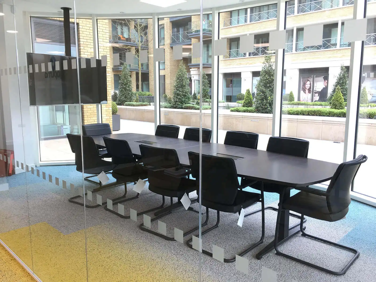 Meeting room with table, black cantilever chairs and TV with High structural glass partition
