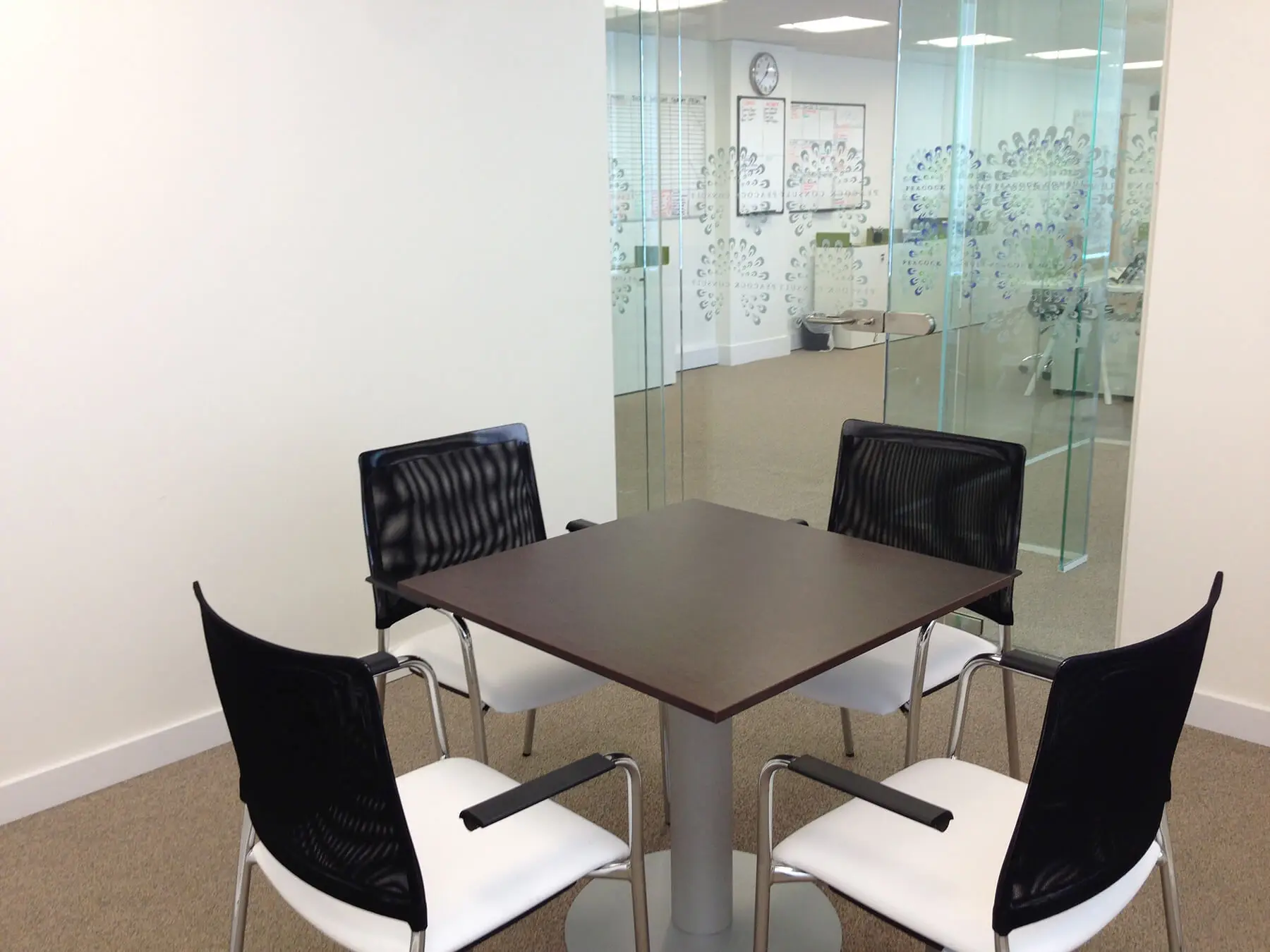 Meeting table with four chairs around it in glass partitioned meeting room